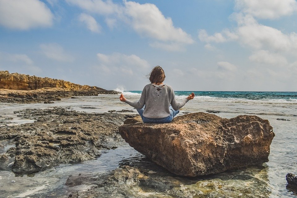 A woman sits on a rock near a beach introspecting and meditating