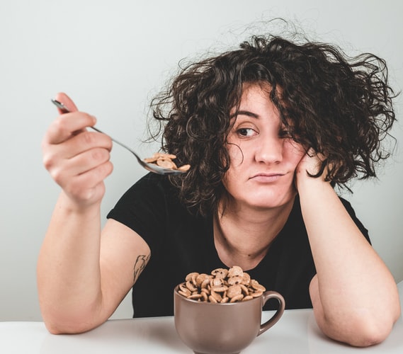 A woman stares at her cereal while looking upset and dissatisfied