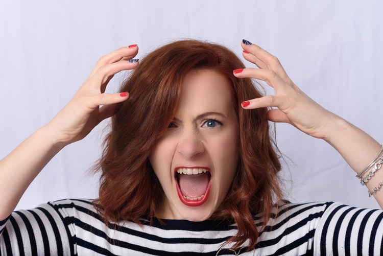 A woman yells with her mouth open and hands near her head, showing exasperation.