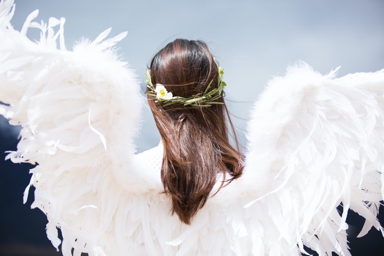 An angel with her face turned away and her wings facing onlookers.