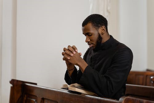 A man prays and reads the bible intently while sitting in a pew