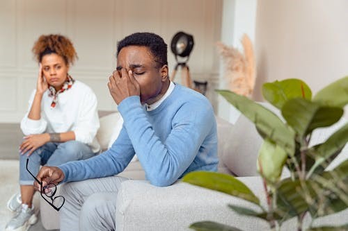 A man and woman sitting on a couch looking upset and distraught